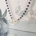 Detailed shot of a black beaded necklace featuring two interlocked golden heart pendants - Double Heart