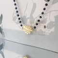 Macro shot of a golden monstera leaf pendant on a black beaded necklace with shadows - Leaf