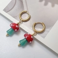 Detalle de pendientes de aro de hongo rojo con motas blancas y ganchos dorados en tarjeta - Pendientes