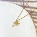 Gros plan détaillé du collier pendentif palmier doré sur socle en marbre blanc - Style Cocotier (DN274)