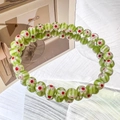 Detailed view of green glass beads with white daisy patterns and red centers on a bracelet - 6MM Green