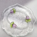 Minimalistisches Perlenarmband mit violetten Tulpenanhängern auf einem Glastablett - Lila