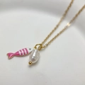 Macro detail of gold necklace with a pink fish charm and a white baroque pearl pendant - Pink