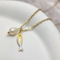 Macro shot of gold stainless steel necklace with freshwater pearl and fish charms - Yellow