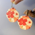 Makroaufnahme von handbemalten floralen Tonohrringen mit 3D-geprägten roten Blüten - Gelb und Orange