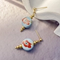 Detail of blue ceramic stud earrings with red floral patterns and gold accents - Blue
