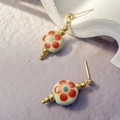 Detailed close-up of pale green ceramic earrings with red floral patterns and gold beads - Green