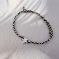 Macro detail of hand-woven black and gold cord bracelet with silver star charm - Steel Color - Star