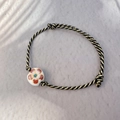 Vista macro detallada de pulsera tejida a mano en negro y oro con cuenta de cerámica - Blanco