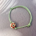 Detalle de pulsera tejida bohemia con cuenta de cerámica crema y diseño floral rojo - Verde