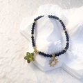 Detail of black beaded bracelet with gold sun charm and green star pendant on white stand - Black - Green Star