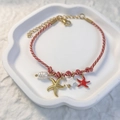 Détail du bracelet tressé rouge avec breloques étoile de mer dorées et perles sur plateau - Rouge