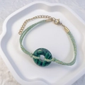 Macro detail of hand-woven green malachite stone bracelet with golden lobster clasp - Peacock