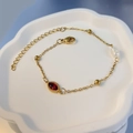 Detailansicht eines vergoldeten Armbands mit rotem Zirkonia und Perle in einer Keramikschale - Oval Rot