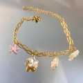 Pulsera de acero inoxidable dorada con estrella y dijes rosas en fondo reflectante - Transparente