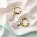 Close-up of geometric gold hoop earrings featuring polished pink quartz stone cubes - Diamond Pattern