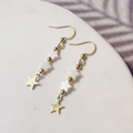 Detail view of gold star dangle earrings with white shell stars on a white display stand - Star Style