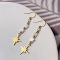 Detail of gold drop earrings featuring white shell stars and North Star charms - Eight-pointed Star Style