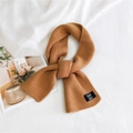 Caramel brown knitted scarf with black label on soft white linen background - Orange