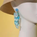 Détail de longues boucles d'oreilles pétales bleues sur un mannequin avec chapeau - Style Nacré Irisé Bleu Ciel (25969 Bleu)
