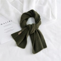 Sciarpa in maglia verde scuro con etichetta in pelle su sfondo di lino bianco - Verde