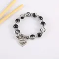 Detail of beaded bracelet with heart pendant, bell, and silver tube on white background - Black