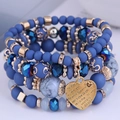 Makro-Detail des mehrlagigen Perlenarmband-Sets mit goldenem Herz-Anhänger Ich liebe Dich - Blau