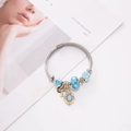 Bracciale in filo d'acciaio argento con ciondoli a cuore blu e pendente dorato D su rivista - Goccia d'Acqua Blu