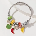 Bracciale a treccia argento con ciondoli a frutta e targhette su supporto bianco - Mela