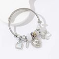 Detail van zilveren gedraaide armband met pompoen koets en hartvormige bedels met stras - Wit