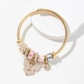 Goldener Armreif mit Perlen-Schmetterling-Anhänger und rosa Perlen auf weißem Sockel - Rosa