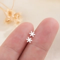 Mini zilveren sneeuwvlok oorknopjes, delicaat sterontwerp vastgehouden tussen de vingers - Zilver