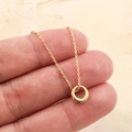 Minimalistische gouden druppel cirkel ketting vastgehouden tegen beige achtergrond - Goud