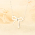 Minimalistische zilveren strik hanger ketting met fijne ketting op een linnen textuur - Zilveren Strikstijl (W29)