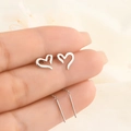 Close-up of silver heart-shaped tassel earrings and studs being held on a soft background - Silver Heart Ear Line (A185)