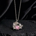 Detalle macro del collar plateado con gema de corazón rosa sobre seda negra y roca volcánica - Estilo Rosa de Corazón Rosado Plateado (K)