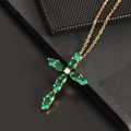 Golden cross necklace with emerald green pear-cut zircon stones on a black texture - Green Gemstone