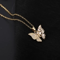 Vue macro du pendentif papillon doré avec pierres en zircone sur fond en tissu noir - Papillon en diamant blanc asymétrique (F)