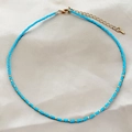 Minimalist turquoise beaded choker necklace with gold accents on soft beige satin - Blue