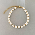 Elegantes Perlenarmband mit weißen Scheiben und Goldperlen auf grauem Hintergrund - Weiß