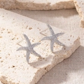 Macro detail of silver starfish earrings with micro-paved zircons on a beige stone base - Starfish Pave
