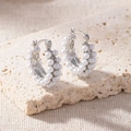Detail shot of silver double-layered hoop earrings with white pearls on a textured stone - Triple Row Pearl Hoop