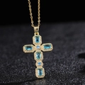 Collier croix dorée avec pierres de zircon bleues et accents de diamants sur fond noir - Style Bleu Clair