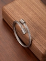 Detail eines gedrehten Edelstahl-Armbands mit polierten Enden auf Holzuntergrund - Silber