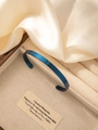 Detail shot of a minimalist gold-plated C-shaped cuff bracelet on a linen display stand - Blue