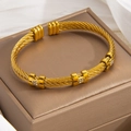 Eleganter goldener gedrehter Armreif mit Diamantakzenten auf einer Schmuckschatulle - Gold