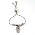 Makro-Detail der silbernen Schlangenkette mit Hamsa-Hand und blauem Evil Eye Anhänger - Stahlfarbe