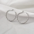 Macro shot of silver geometric hoop earrings with textured chain link design on white velvet - Silver