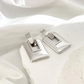 Detailaufnahme silberner geometrischer Rechteck-Ohrringe auf weißem Stein und Seide - Silbernes Quadrat