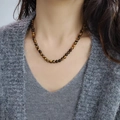 Tijgeroog kralenketting met natuurlijke goudbruine stenen op een grijs vest model - 6mm Tijgeroog Ketting